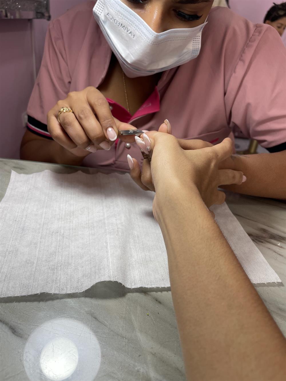 Manicurista con uniforme rosado trabajando las uñas de una clienta